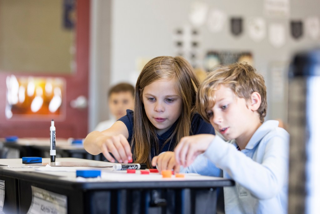 Two students collaborate on a math problem using math manipulatives and mini whiteboards. 