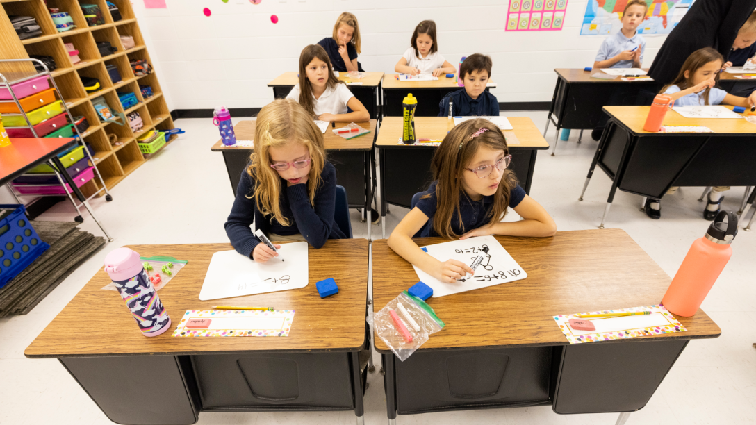 Students in a classroom using mini whiteboards to solve addition problems and understand number bonds.